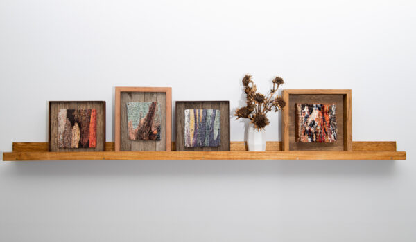 Four framed tapestries side by side on a shelf. Each tapestry is a close up view of tree bark.