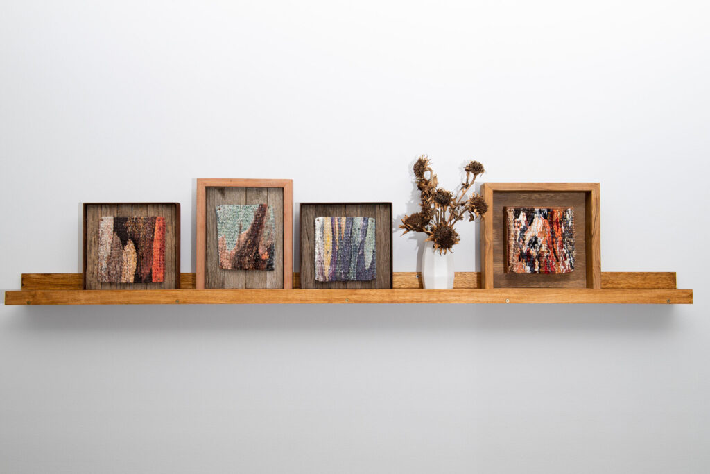 Four framed tapestries side by side on a shelf. The tapestries are new work from Lee Leibrandt's Specere collection. Each tapestry is a close up view of tree bark. 