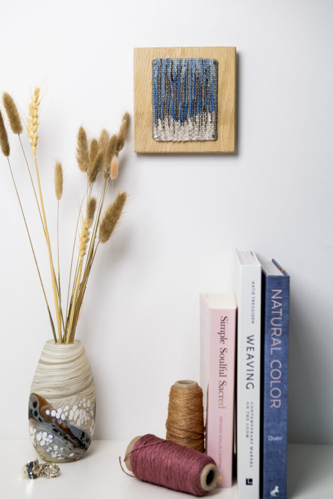 Winter tapestry hanging above books and vase