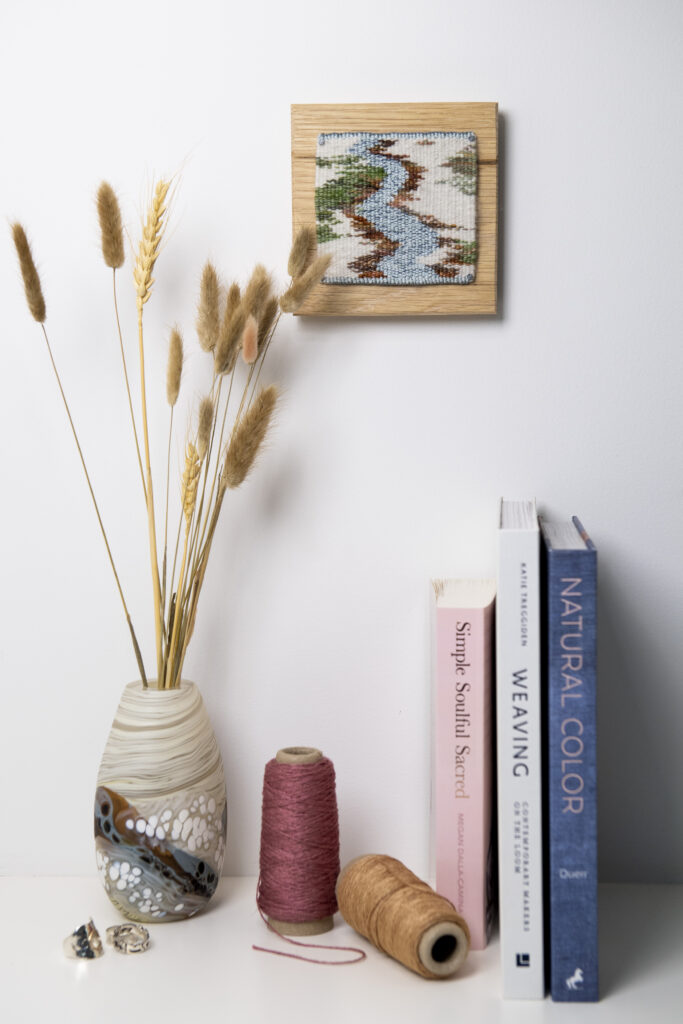 A winter tapestry hangs above books and a vase