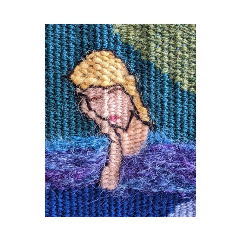 A close up of a woven image of a woman with blonde hair and fluffy blue jumper. She is resting her head on her hand.