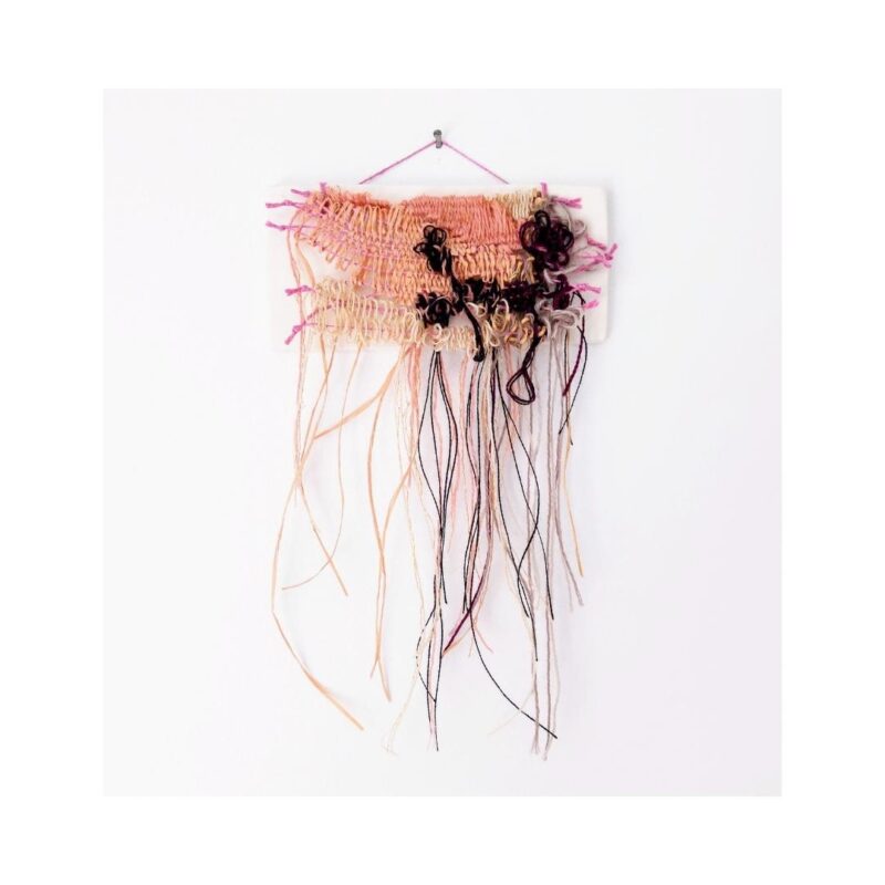 A tiny, frayed tapestry in pink and black. Mounted to a white ceramic tile.
