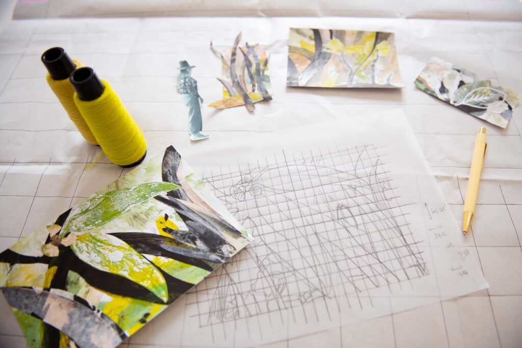 Various collages of ecalyptus woodlands are arranged on a table, with a pencil tracing of one design in the foreground.
