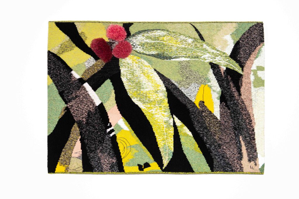 Eucalyptus leaves in shades of green and yellow feature in front of blackened tree shapes. Three blossoms in pink and red are toward the top of the tapestry.